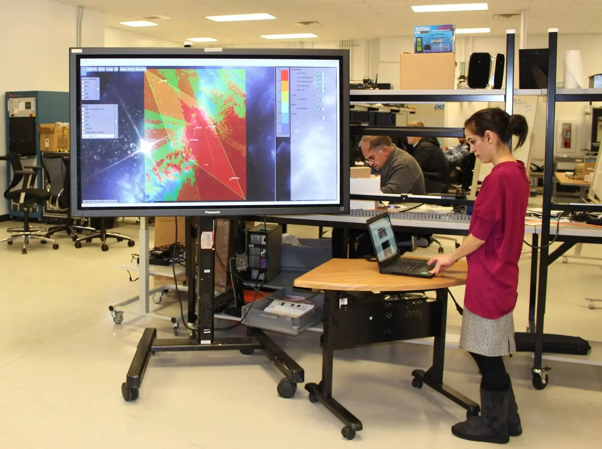 Engineer demonstrating a planning tool on a large simulation display in a modeling and simulation lab