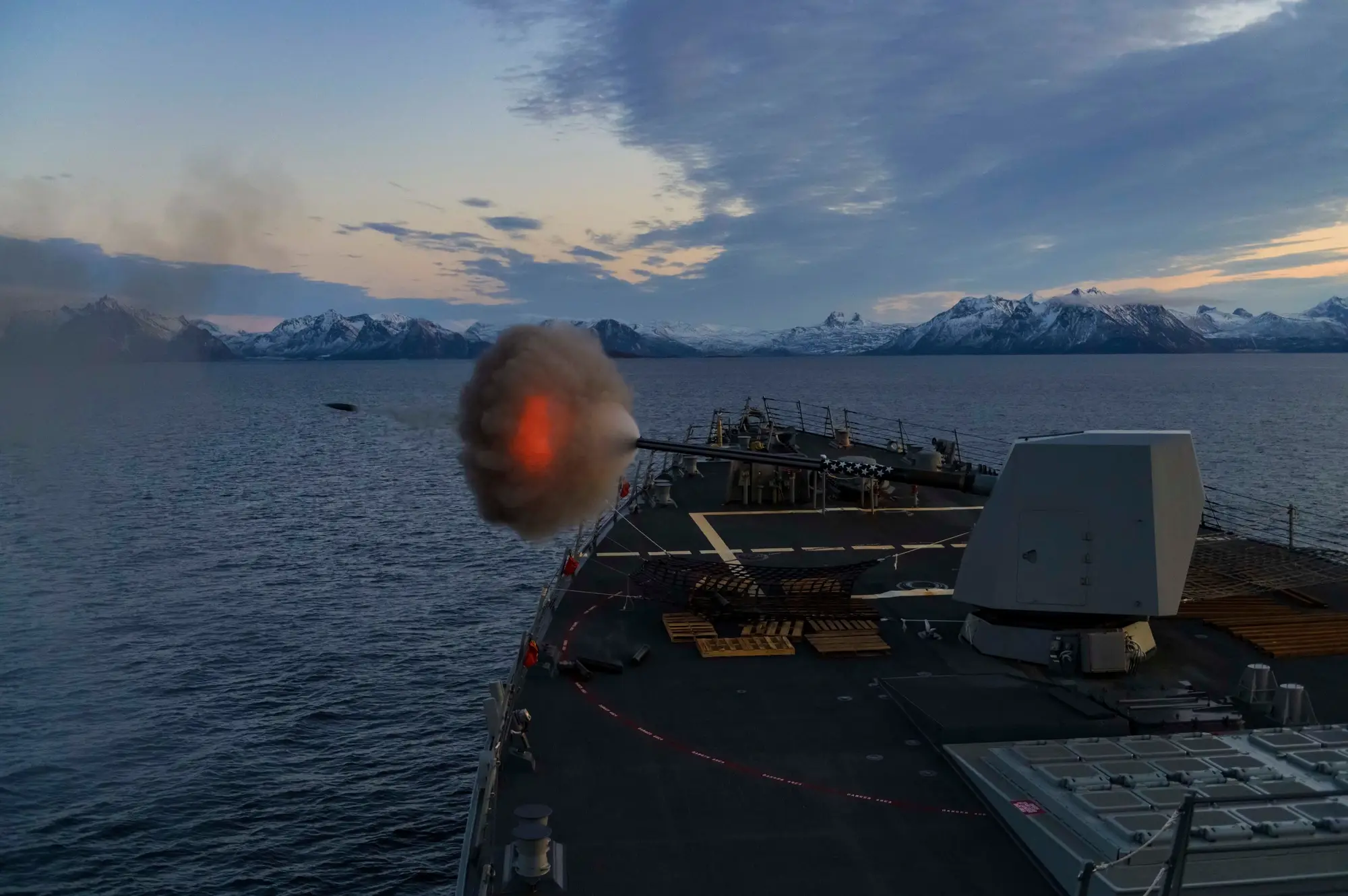 Destroyer firing its 5-inch deck gun at dusk during a live-fire exercise