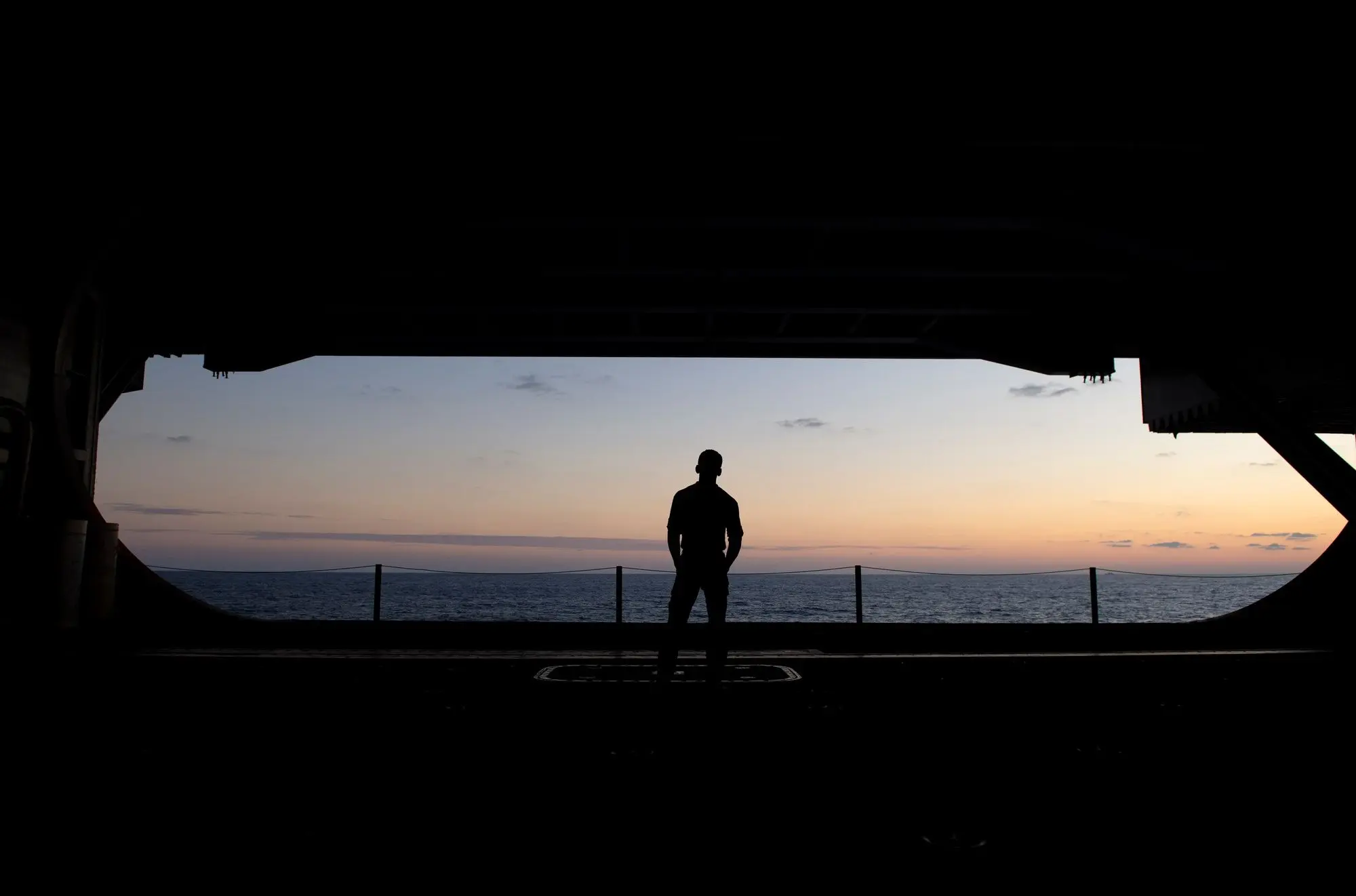 Sailor silhouetted in an open hangar bay door at sunset