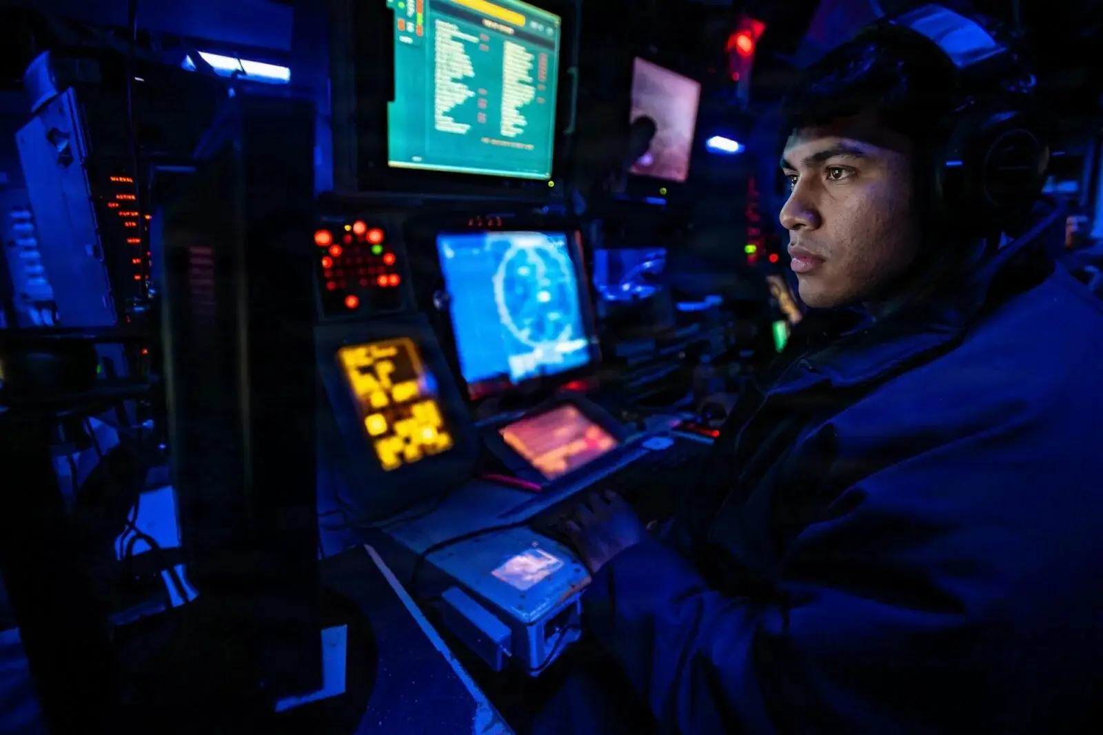 Sailor standing watch at glowing radar and combat system screens in a destroyer combat information center